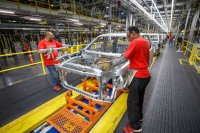 Two workers on a car assembly line working on the vehicle body.