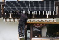 A man installs balcony solar panels on an apartment balcony in Germany