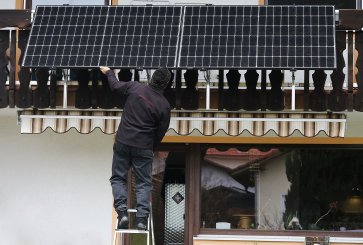 A man installs balcony solar panels on an apartment balcony in Germany