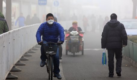 Man wearing a face mask rides a bicycle on a foggy day.