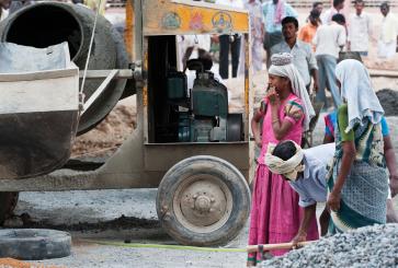 Construction workers in colorful clothes stand near a cement mixer.