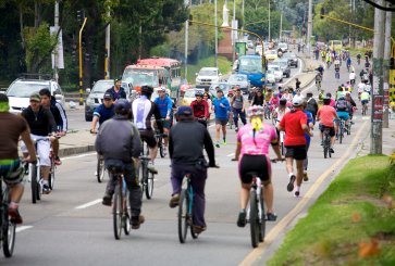 People ride bikes and run on one side of a street while cars move on the other side.