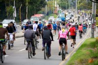 People ride bikes and run on one side of a street while cars move on the other side.