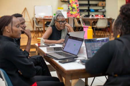 People sit around a table, with their laptops, during a meeting.