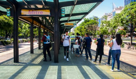 People waiting in the shade of a bus stop shelter.