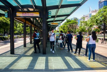 People waiting in the shade of a bus stop shelter.