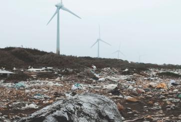 A beach littered with trash and windmills in the background.