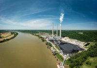 Aerial view of a power plant on a river with piles of coal and smoke rising from smokestacks.