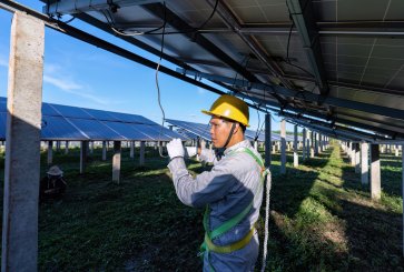 A worker connecting electrical cords beneath a solar panel.