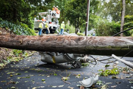 Electrical workers are seen behind a down powerline and pole in the roadway.