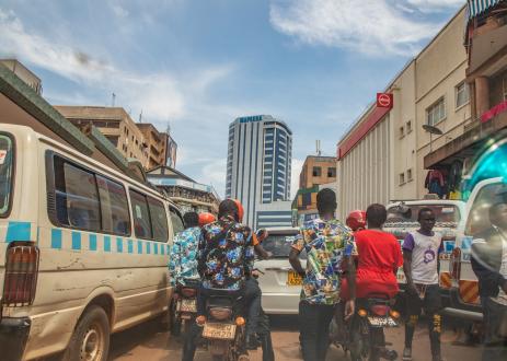 Busy street between buildings with vans, cars, motorcycles, and pedestrians