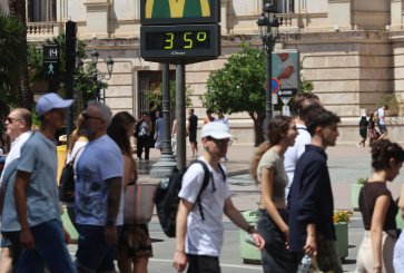 A group of people walks in front of a digital city thermometer reading 35 degrees celsius.