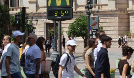 A group of people walks in front of a digital city thermometer reading 35 degrees celsius.