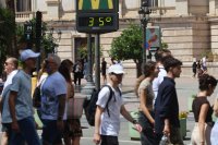 A group of people walks in front of a digital city thermometer reading 35 degrees celsius.