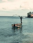Man casting fishing net from small boat.