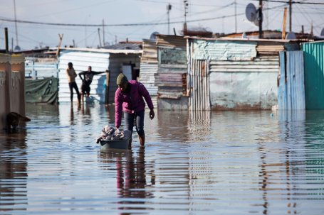 A man floats a laundry basket down a flooded street in a slum.