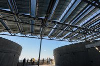 People standing on a rooftop under an elevated solar panel array.