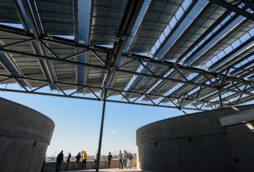 People standing on a rooftop under an elevated solar panel array.