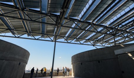 People standing on a rooftop under an elevated solar panel array.