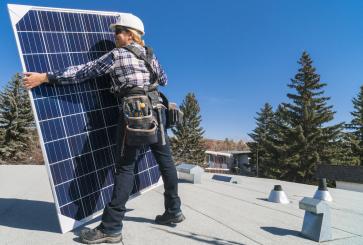 Technician wearing safety hat and carrying solar panel