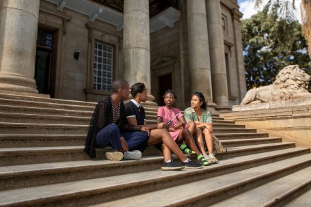 Four people sit on the front steps of the McMillan Memorial Library.