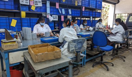 Supply chain workers assemble components while sitting around a long table.