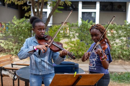 Two music students playing the violin in an outdoor courtyard.