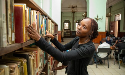 A woman looks through books on a shelf.