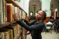 A woman looks through books on a shelf.