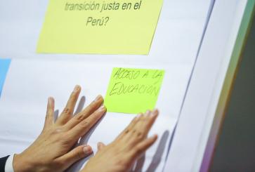 A post-it note that translates to "access to education" is added to an easel during a workshop.