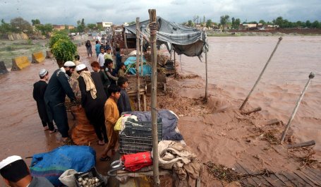 People stand on a mud road with flood waters lapping on either side.