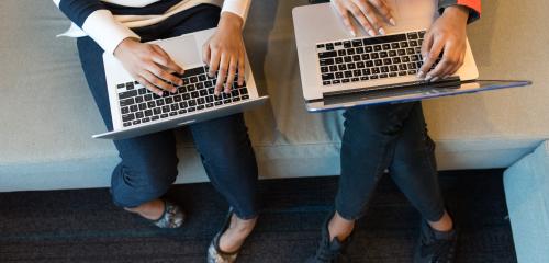 two people's hands working on laptops