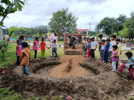 Children stand around a sand pit. 