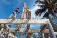 Two construction workers on top of the skeleton of a house.