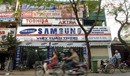 People on motorcycles ride past a Samsung store in Vietnam.