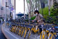 A woman holds onto a yellow shared bicycle.