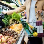 Woman with shopping basket selecting produce.