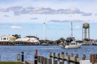 A wind turbine is seen across the water near homes.