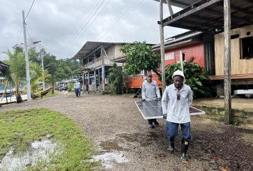 Two people carrying a solar panel down a dirt road. 
