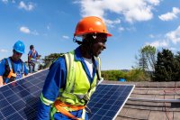 Three people installing a solar panel on a roof.