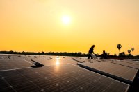 Two workers install solar panels on the corrugated metal roof of a shop.