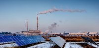 Solar panels with smoke from a smokestack in the background.