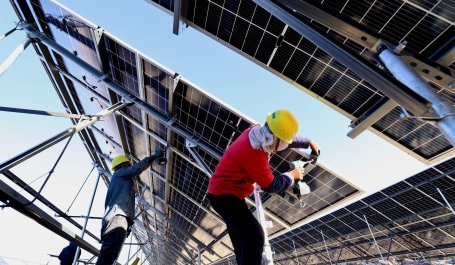 Two technicians installing solar panels on a large metal frame. 