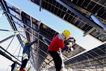 Two technicians installing solar panels on a large metal frame. 