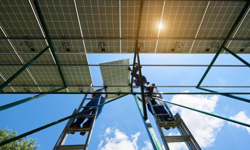 Workers on ladders installing solar panels.