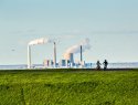 View of two mountain bikers on a grassy hillside with a coal plant in the distance.
