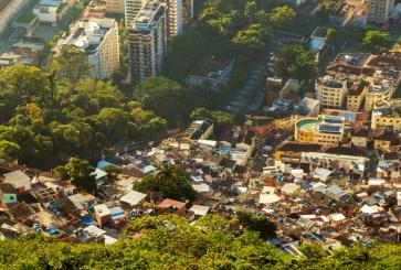 An aerial view of a cluster of small homes next to luxury buildings, all surrounded by trees.