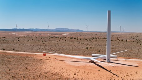An incomplete wind turbine in the New Mexico desert with a row of wind turbines in the background.