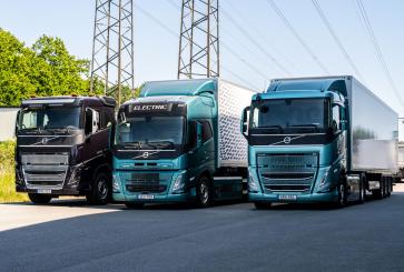 Three zero-emission trucks parked on the street with powerlines and trees.